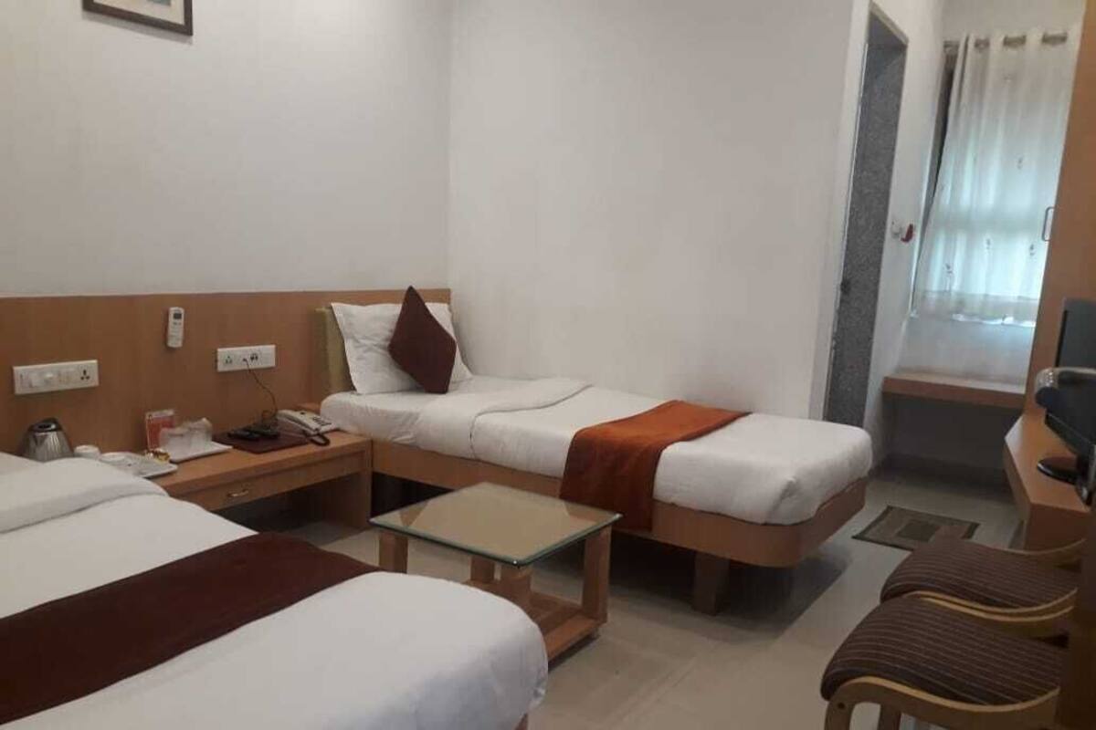 A hotel room with two beds, a small table, a chair, a desk, and a window with curtains.