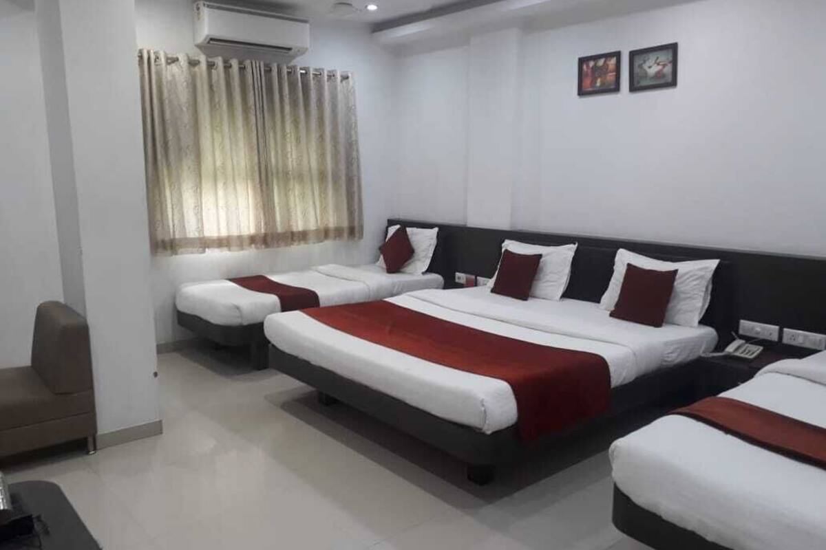 A hotel room with three beds, a sofa, an air conditioning unit, and a window with curtains.
