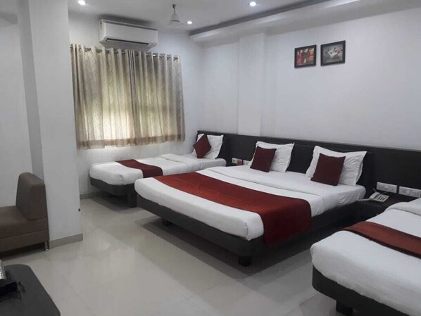 A hotel room with three beds, a sofa, an air conditioning unit, and a window with curtains. - Hotel Harmony (Vadodara)