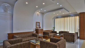 Un'area lounge moderna con divani, un tavolino in vetro, una ventola a soffitto e un'ampia finestra con persiane verticali.