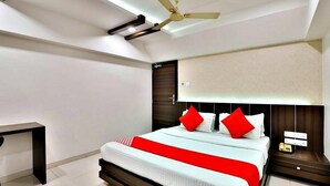 A modern bedroom with a bed, a nightstand, a desk, and a ceiling fan. - Hotel Amber (Vadodara)