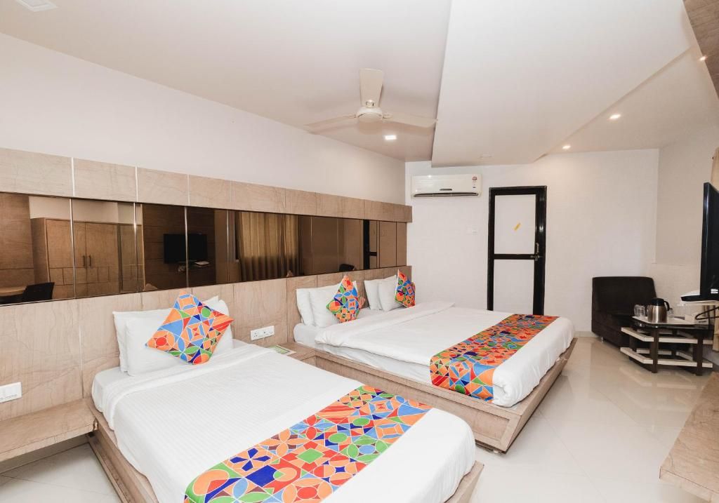 A hotel room with two beds, a ceiling fan, an air conditioning unit, and a small table with a chair.