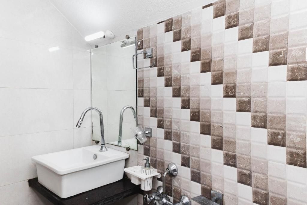 Une salle de bain avec un lavabo blanc, deux robinets, un miroir et un mur de douche recouvert de carreaux.