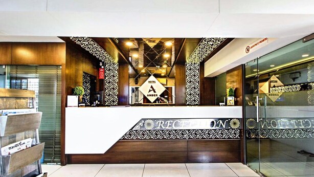 A hotel reception area with a modern design, featuring a reception desk, patterned wall decorations, and a glass partition. - Hotel Amber (Vadodara)