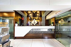 Zona de recepción de hotel con diseño moderno, que incluye un mostrador, decoraciones murales con diseños y una partición de vidrio.