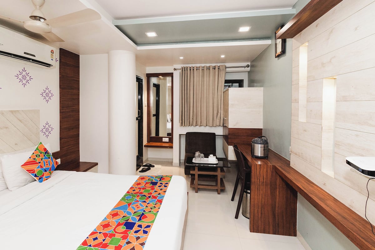 A hotel room with a bed, a desk, a chair, a small table, a heater, and a mirror.