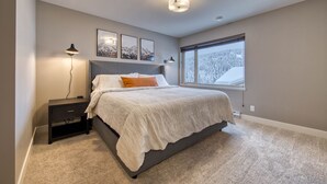 A bedroom with a bed, a nightstand, a lamp, and a window with a view of snow-covered trees. - Cozy Ski-In/Ski-Out Escape: 3BR Echo Landing Home Near Orient Chairlift Sleeps 7 (Sun Peaks)