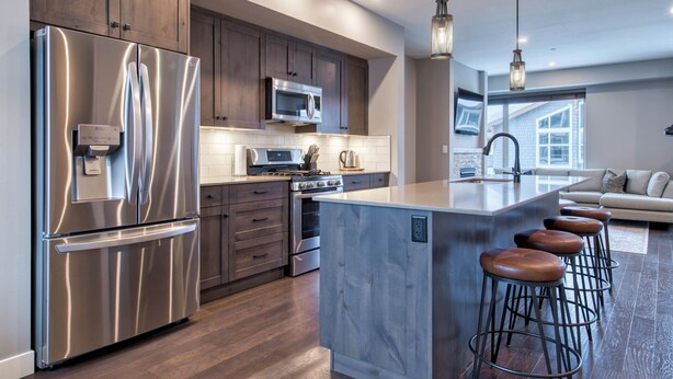 A modern kitchen with stainless steel appliances, wooden cabinets, and a central island with bar stools. - Cozy Ski-In/Ski-Out Escape: 3BR Echo Landing Home Near Orient Chairlift Sleeps 7 (Sun Peaks)
