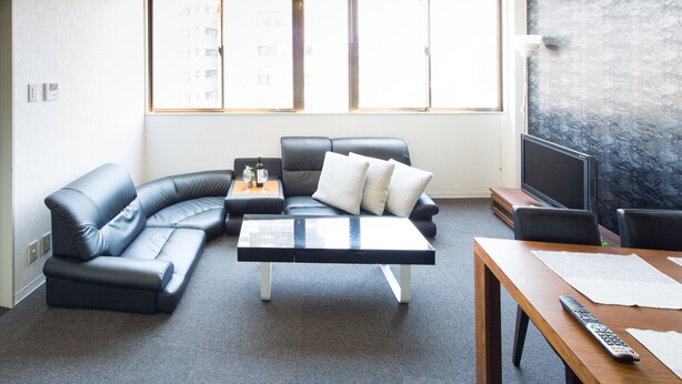 A modern living room with a curved black leather sofa, a glass-top coffee table, and a wooden dining table. - Sakamoto Building 6F (Osaka)