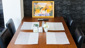 A dining table with placemats, a remote control, a small plant, and a framed picture on the wall. - Sakamoto Building 6F (Osaka)