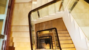 Un interior moderno con una escalera de vidrio y metal, suelo de mármol y vista a un nivel inferior.