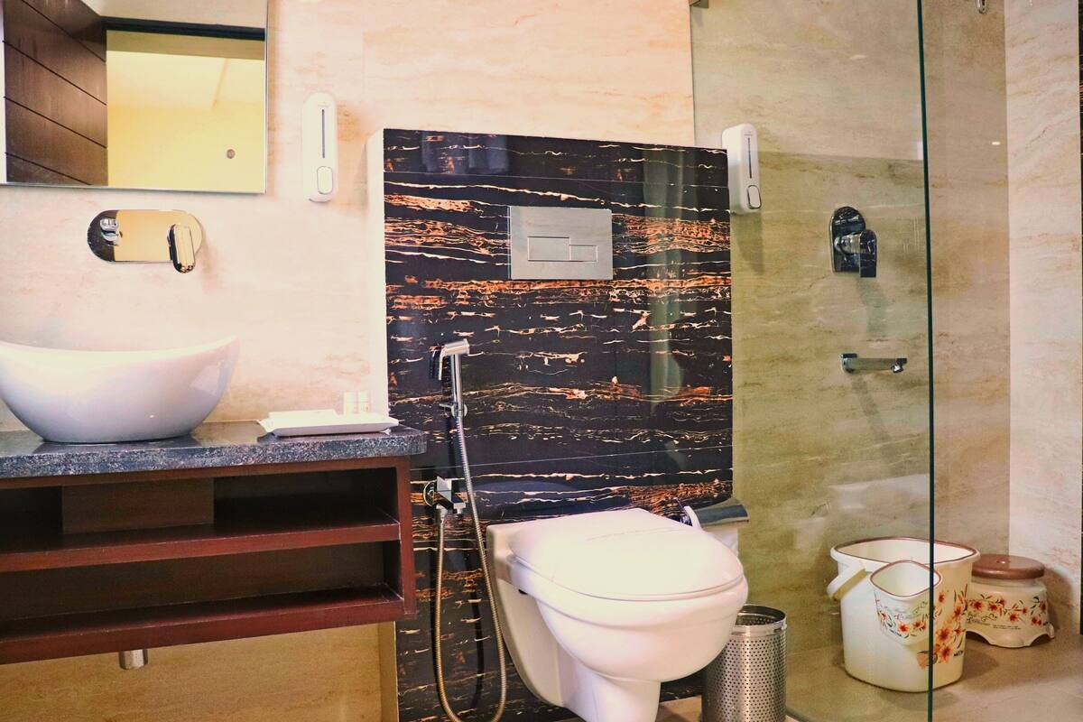 A bathroom with a marble backsplash, a white sink, a toilet, a shower, and a mirror.