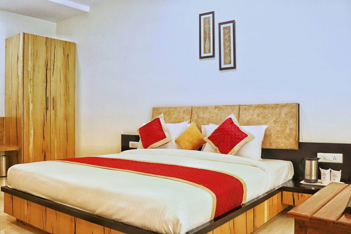 A hotel room with a wooden bed frame, a red and white bedspread, and a wooden nightstand with a kettle.