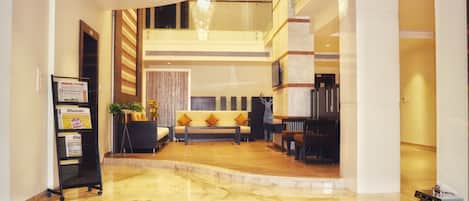 A spacious lobby with a marble floor, a sofa with cushions, a bookshelf, and a staircase leading to an upper level.