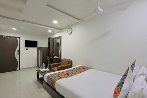 Una habitación de hotel con una cama, un escritorio, una silla, un televisor y un ventilador de techo.