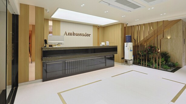 Zona de recepción con mostrador identificado como "Ambassador", diseño moderno con paneles de madera y un pequeño jardín interior.