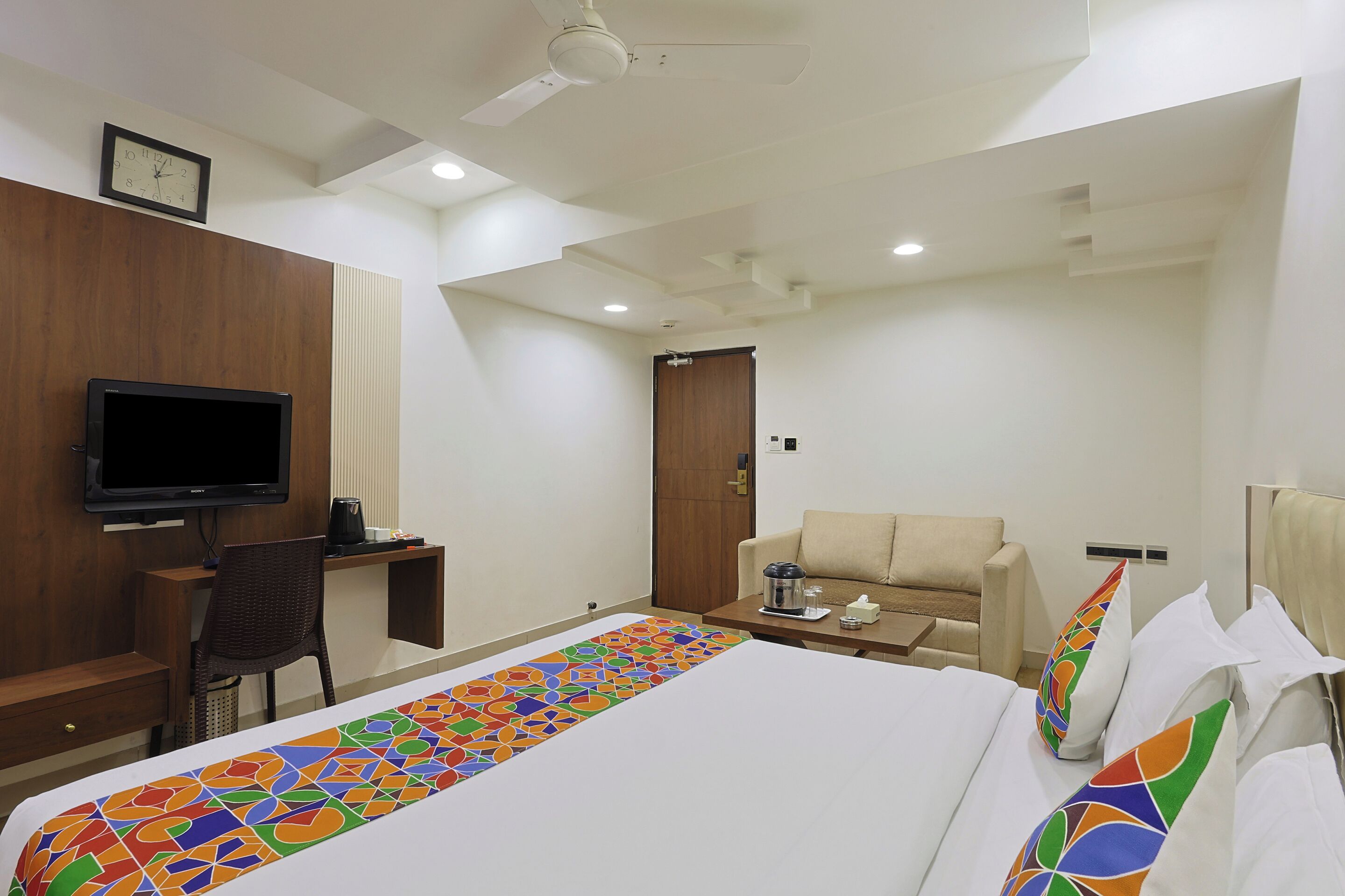 A hotel room with a bed, a desk with a TV, a chair, a sofa, and a coffee table.