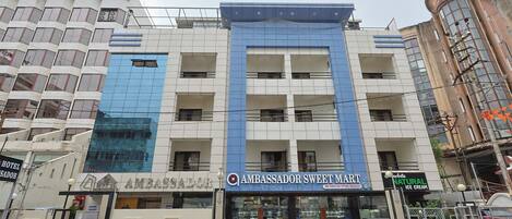 Ein mehrstöckiges Gebäude mit einem zentralen Eingang, einem Schild für 'AMBASSADOR SWEET MART' und einer sichtbaren Schaufensterfront mit Glasfassade.
