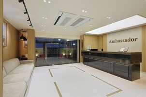 A reception area with a reception desk labeled "Ambassador," a seating area with a sofa, and a glass door leading outside.