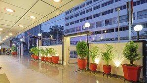 Vestíbulo de hotel con piso mojado, plantas en macetas y una entrada bien iluminada.