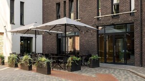 An outdoor seating area with tables and chairs, surrounded by planters with greenery. - Wellton Riverside SPA Hotel (Riga)