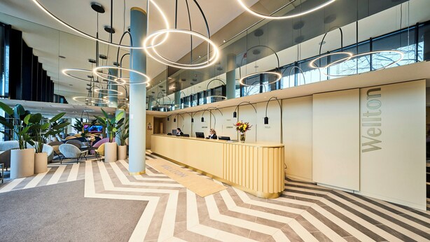 A modern hotel lobby with a reception desk, seating area, and a large staircase.