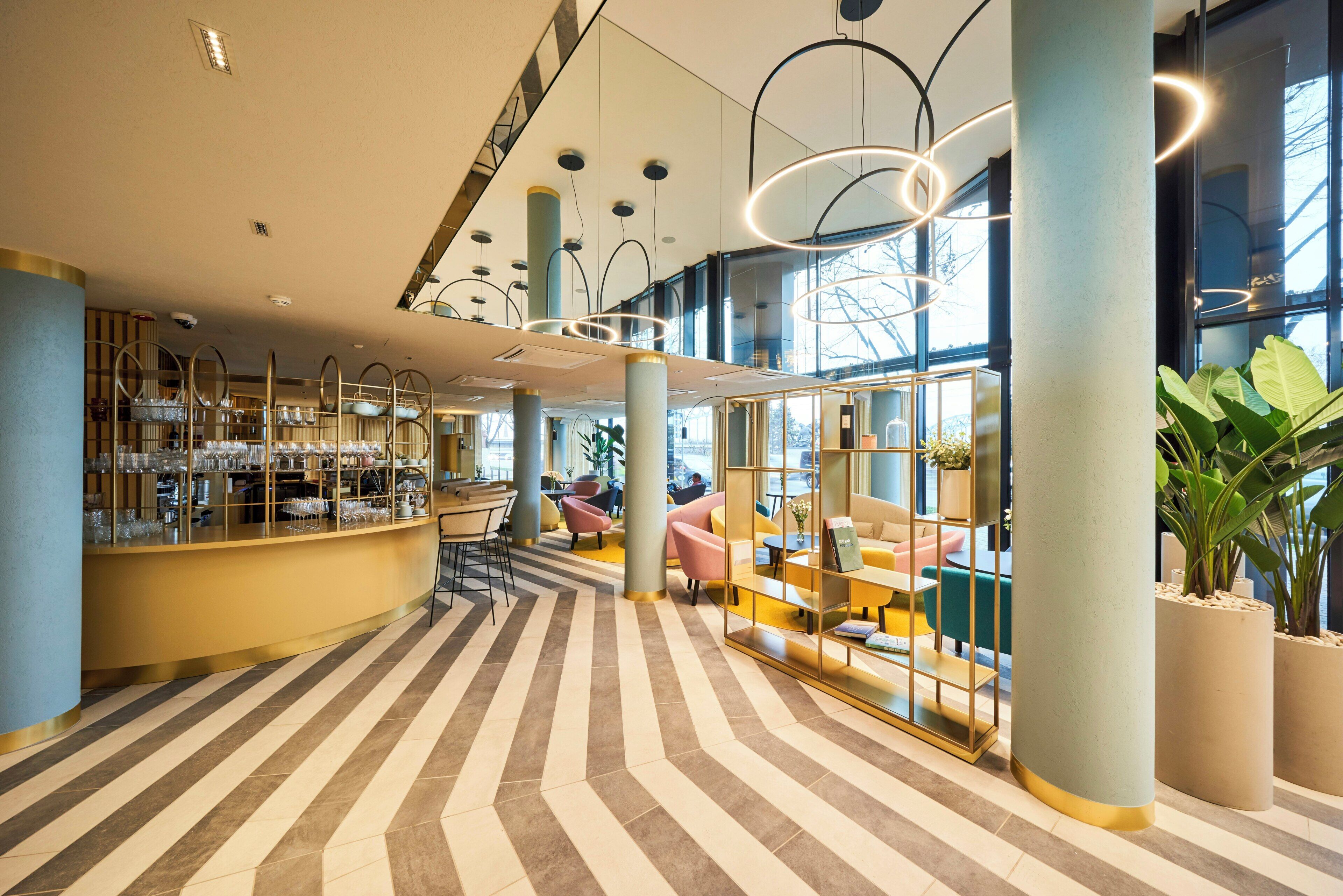 A modern hotel lobby with a bar area, seating, and large windows.