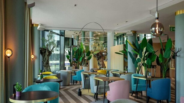 A modern interior with round tables and chairs, large potted plants, and a chevron-patterned floor. - Wellton Riverside SPA Hotel (Riga)