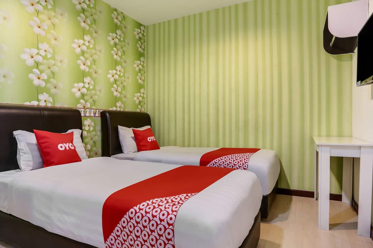 A hotel room with two beds, each with a red and white bedspread, a black headboard, and a red pillow with the logo "OYO". The room has green striped wallpaper and a small white table.