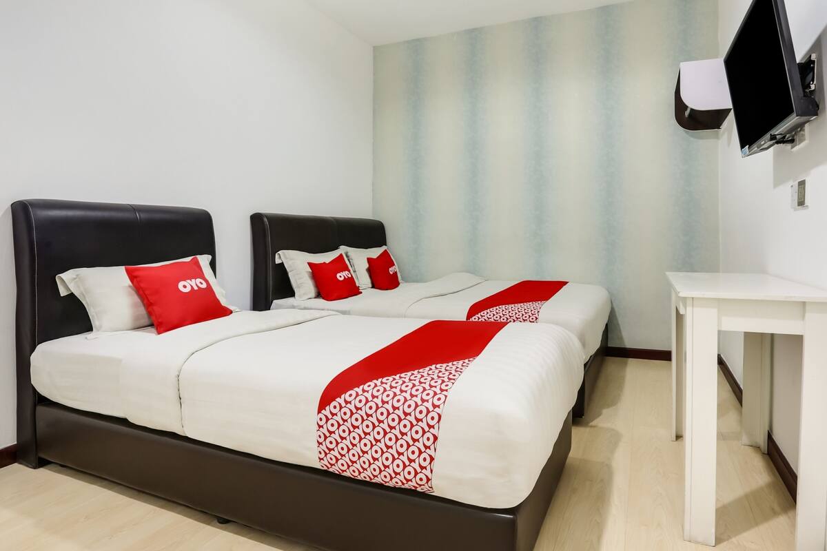 A hotel room with two beds, a desk, and a TV mounted on the wall.