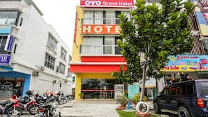 A hotel with a prominent red and yellow facade, a parking area with motorcycles, and a small tree in the foreground. - OYO 89583 Grove Hotel (Kajang)