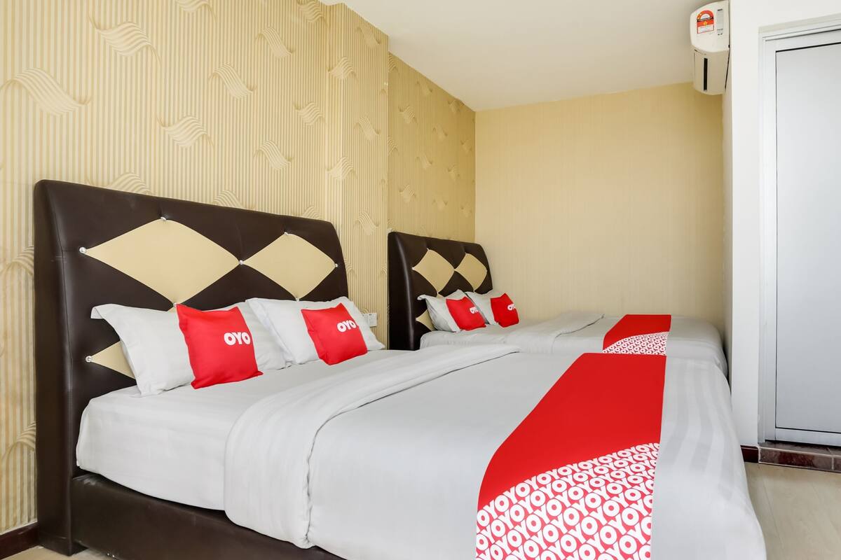 A hotel room with a bed, two nightstands, a wall-mounted air conditioner, and a door.