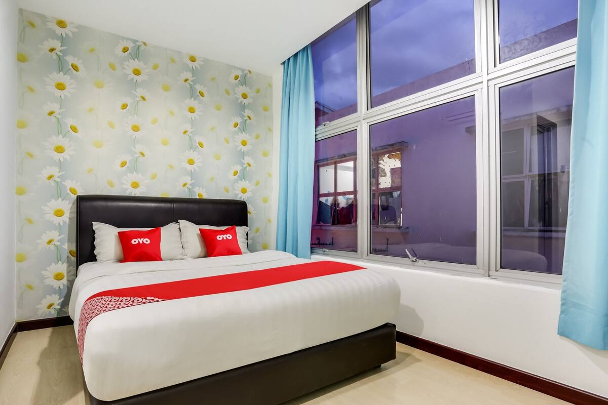 A hotel room with a large bed, a window with curtains, and a wall with a daisy pattern.