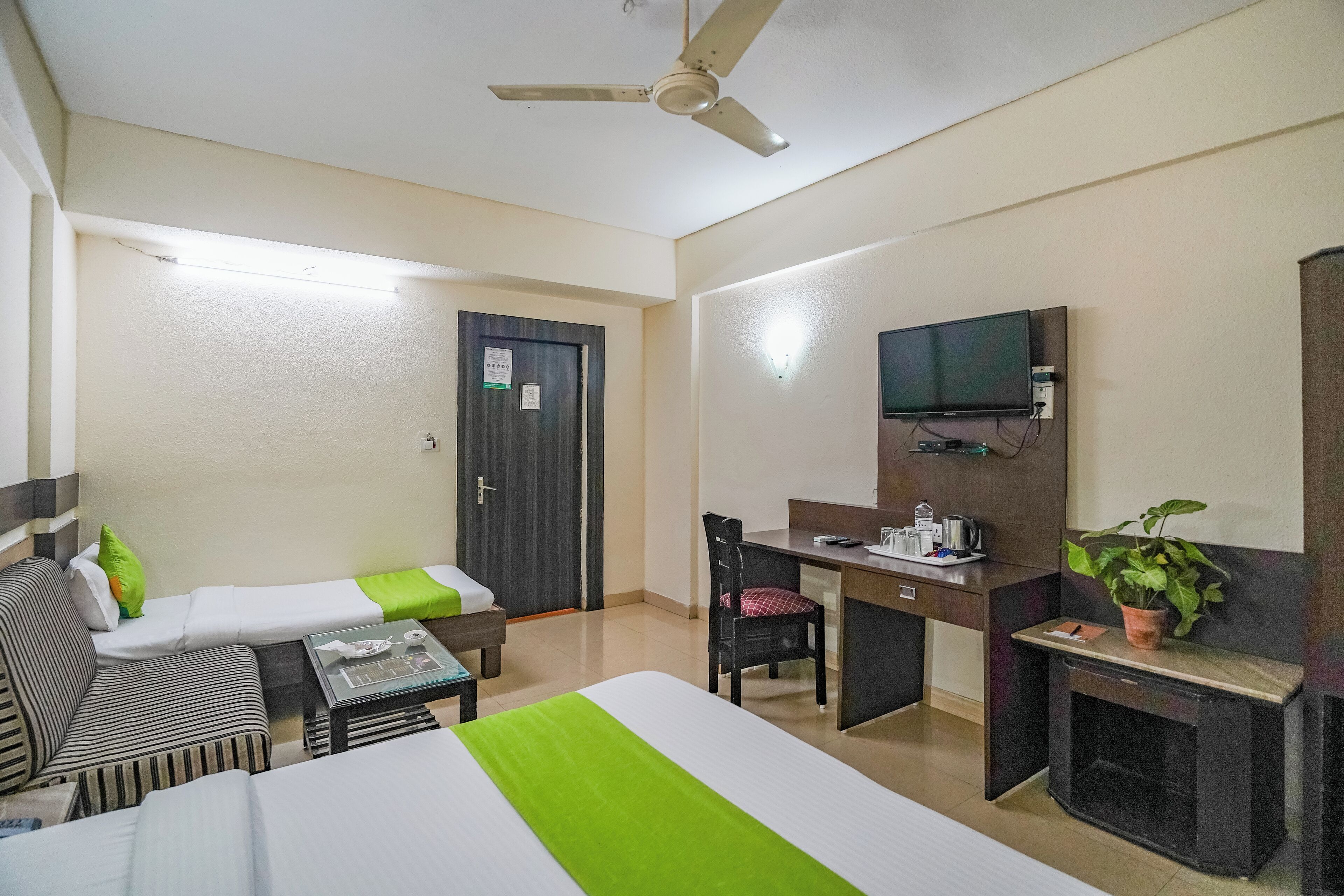 Une chambre d’hôtel avec deux lits simples, un bureau avec une chaise, une télévision et un ventilateur de plafond.