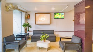 Una sala de estar moderna con un sofá gris, dos sillones, una mesa de centro con una planta, un televisor en la pared y un cuadro grande enmarcado.