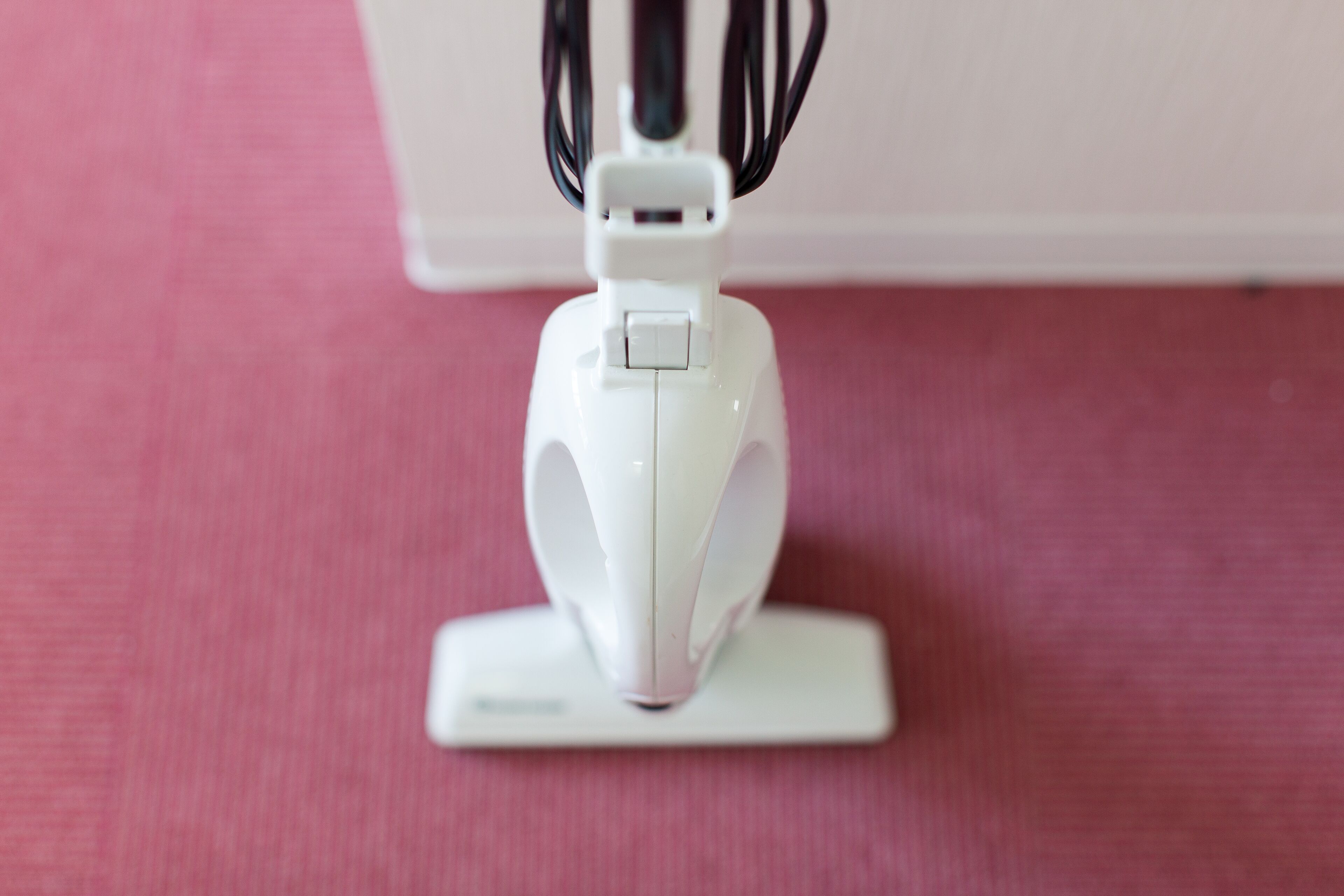 A white electronic device on a white base, likely a charging station, on a pink surface.