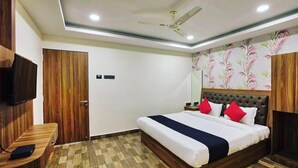 Quarto de hotel com cama, televisão, escrivaninha e ventoinha no teto.