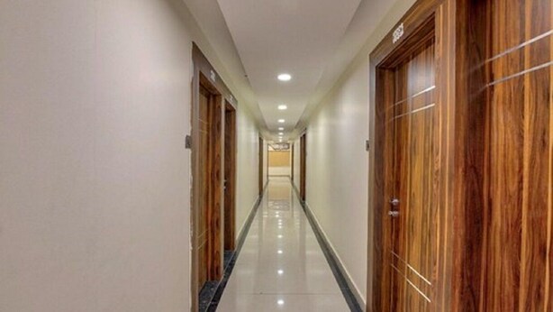 Corredor longo e estreito de um hotel, com portas de madeira em ambos os lados e um chão de azulejos brilhantes.