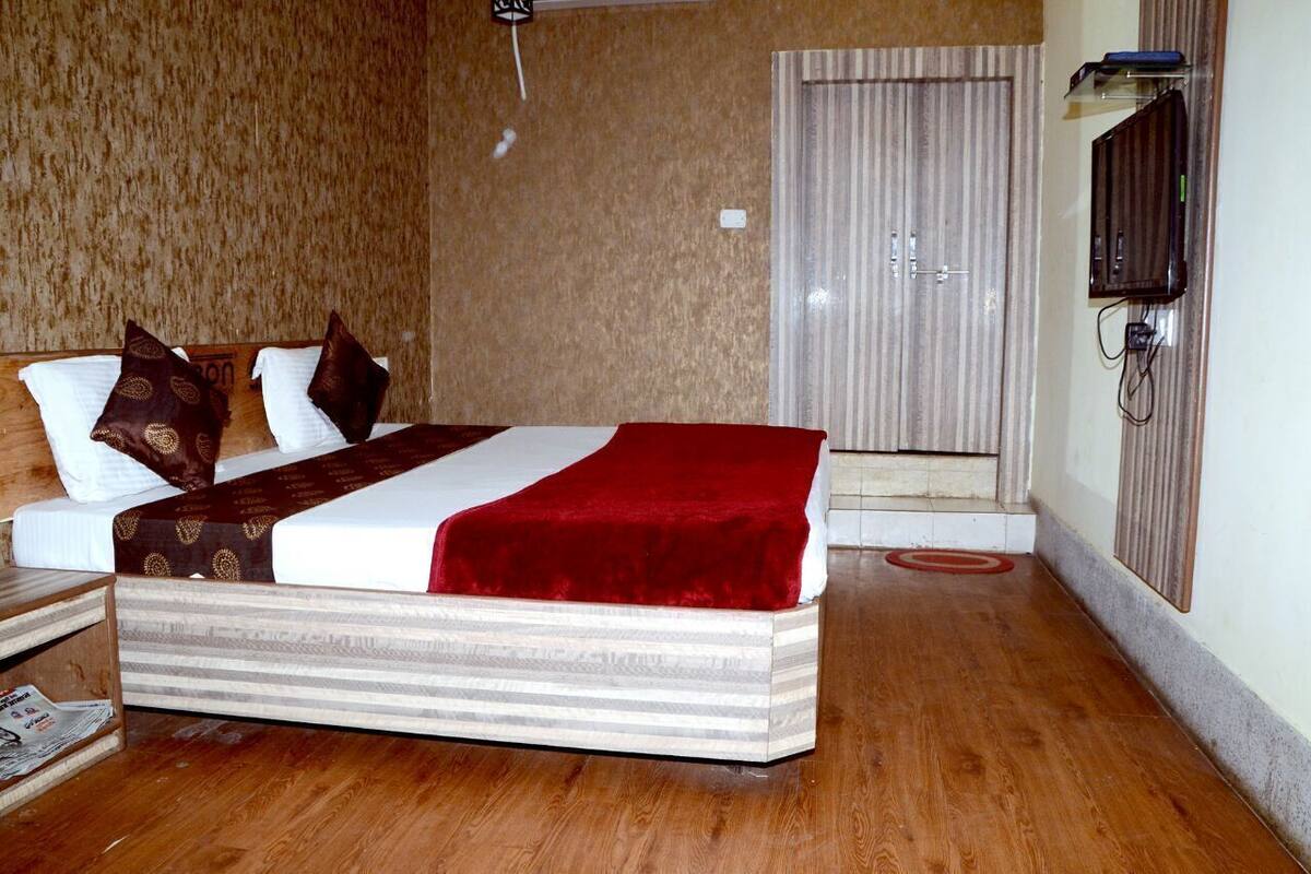 A hotel room with a bed, a television, a door, and a wooden floor.