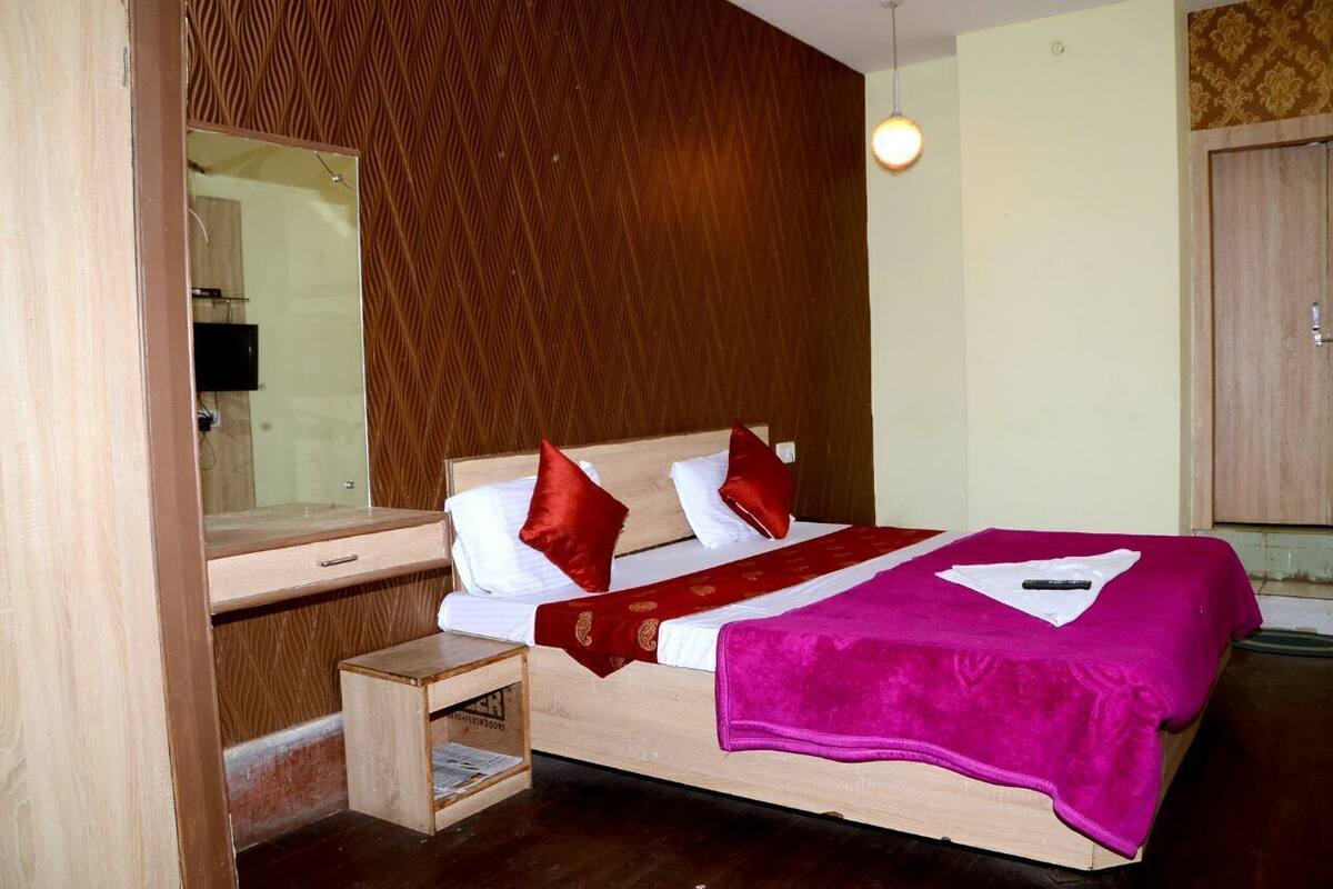 A bedroom with a wooden bed, a bedside table, a mirror, and a hanging light fixture.