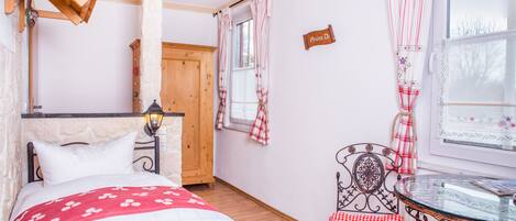 Un dormitorio con una cama, un armario de madera, una mesa con una silla y un ventanal con cortinas.