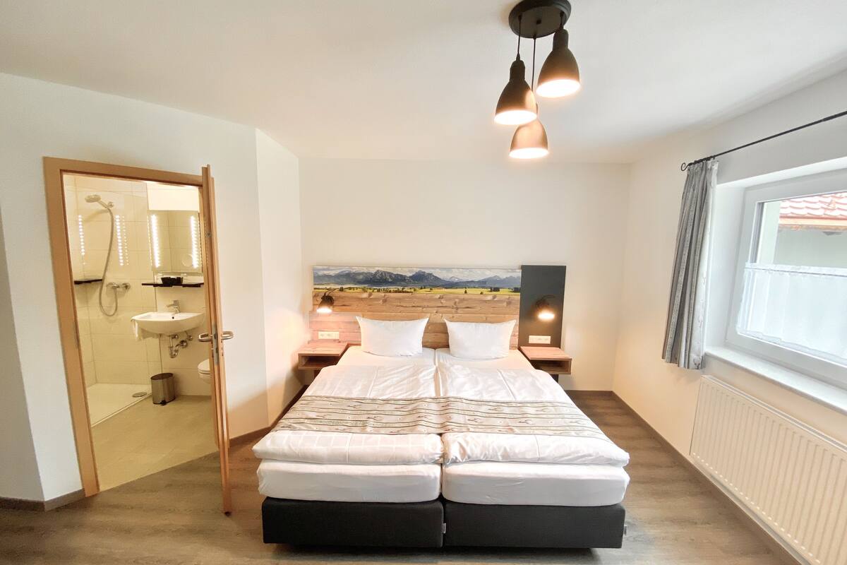 Ein Schlafzimmer mit einem Bett, einem hölzernen Kopfteil, einem Nachttisch, einem Spiegel, einem Fenster und Bergblick.