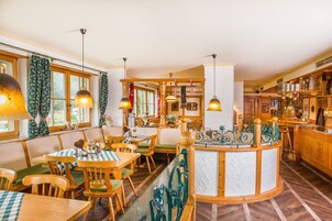 Un restaurante acogedor con muebles de madera, manteles a cuadros verdes y blancos, y lámparas colgantes.