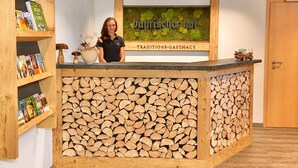 Een receptiebalie met een houten blad en een wanddecoratie met 'bayrischer Hof' en 'TRADITIONS-GASTHAUS'.