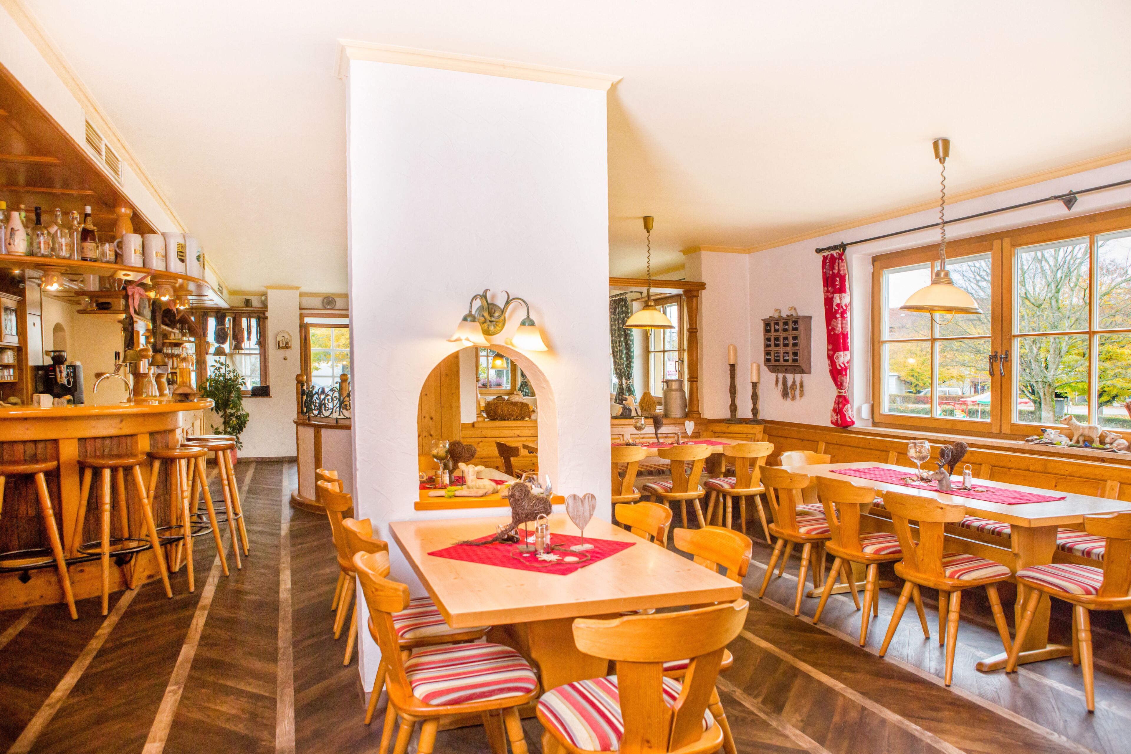 A cozy restaurant with wooden furniture, a central bar area, and large windows offering a view of the outdoors.