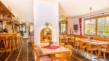 A cozy restaurant with wooden furniture, a central bar area, and large windows offering a view of the outdoors.