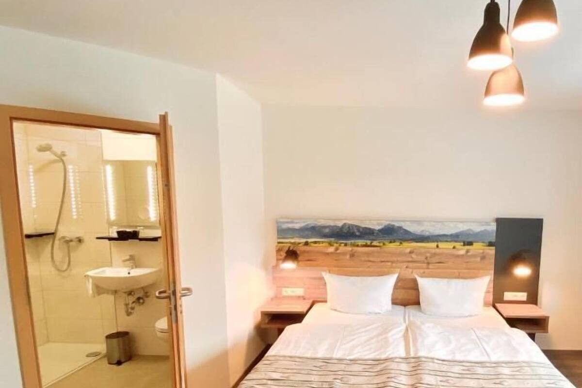 Ein Schlafzimmer mit Bett, einem Landschaftsbild, einer Dusche und einem Waschbecken.