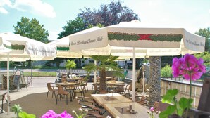 Een terras met tafels en stoelen onder parasols, omgeven door bloemen.