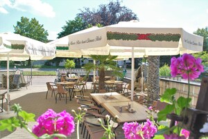 Café al aire libre con mesas y sillas bajo sombrillas, rodeado de flores.