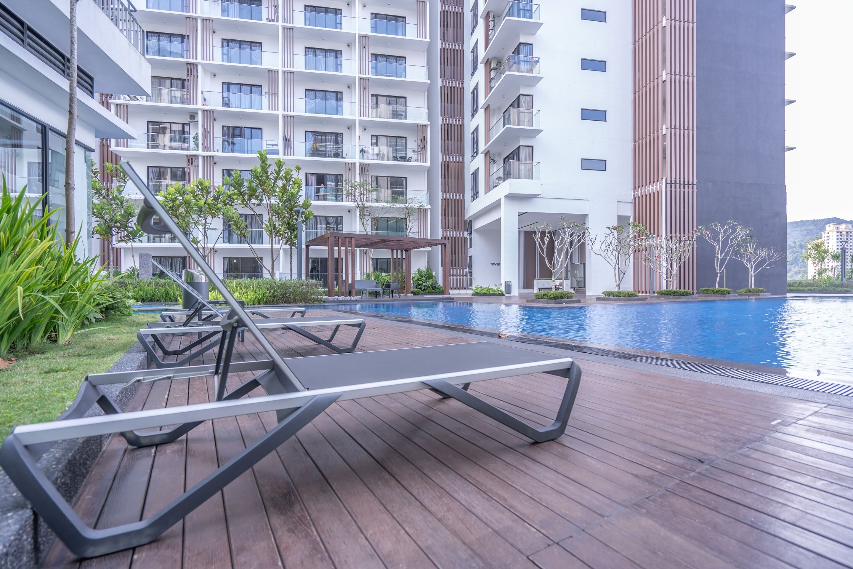 A modern hotel with a swimming pool, lounge chairs, and a covered seating area.